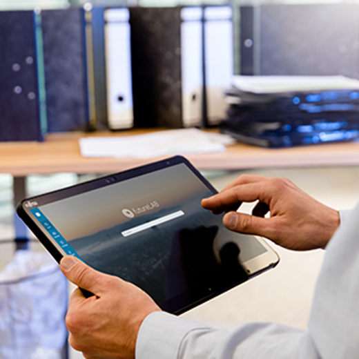 A Person Using A Tablet To Log Into A Digital Platform, Surrounded By Organized Filing Cabinets And Stacks Of Documents.
