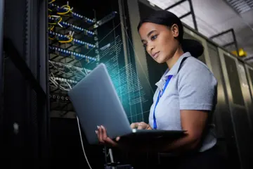 Woman in data center in front of open server rack holding laptop