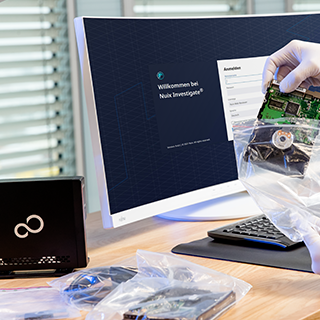 A Hand In A Glove Holds A Circuit Board Over A Computer Monitor Displaying A Welcome Screen For Neuk Investigate, With Equipment Nearby.