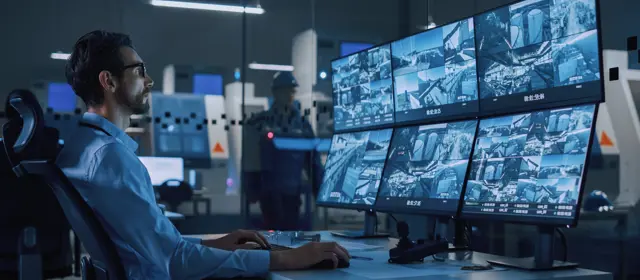 Man Sitting In Front Of Monitors Showing Surveillance Camera Feeds