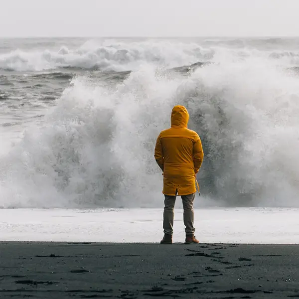 Person On The Beach Looks At A Large Breaking Wave
